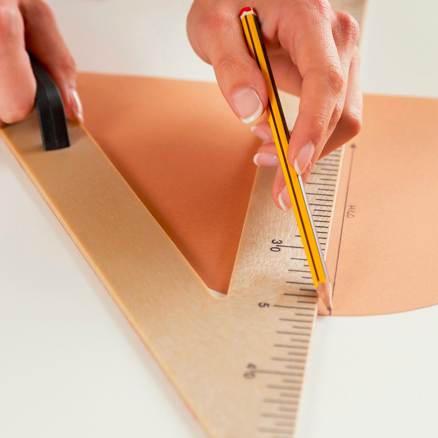 Person measuring leather with a ruler and pen on a white background
